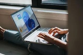 A person working on Windows 11 laptop on the couch the screen is blue and it is showing widgets