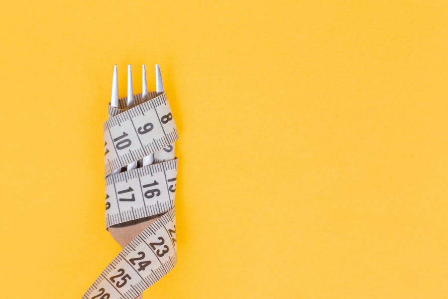 A weight loss measuring tape wrapped around a fork on a yellow surface