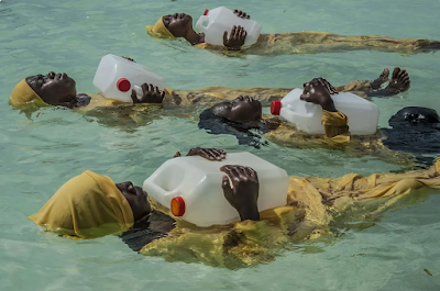 women in colorful yellow burkinis learn to float in the Indian Ocean by holding large empty water jugs