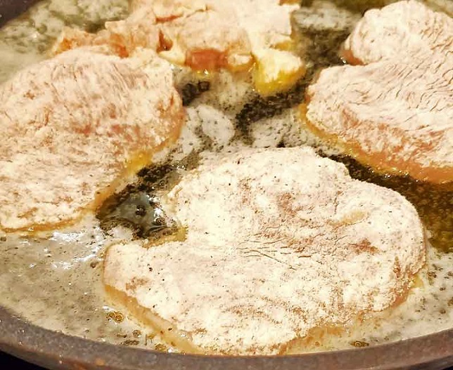 flour and seasoned chicken cutlets frying in butter