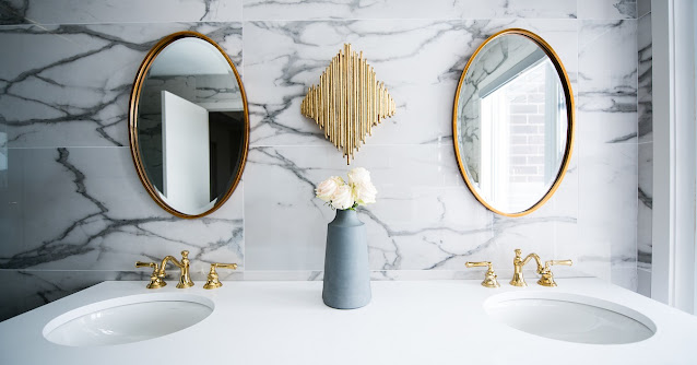 Gold sink fixtures in a marble bathroom with gold framed mirrors.