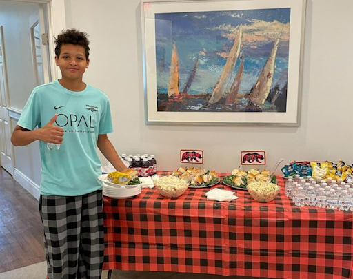 boy with thumbs up standing in front of table of food