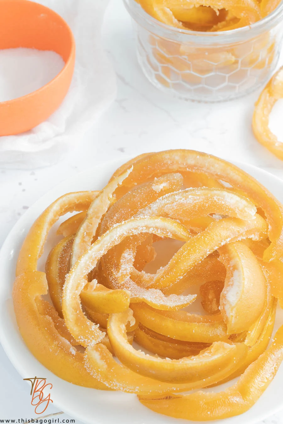 A picture of dried pomelo peel on a white plate with an orange bowl of sugar