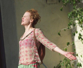 Nicole Kidman with curly red hair, wearing a floral pink blouse, stands in the sunlight with her arms outstretched, eyes closed, and a joyful expression. Aesthetic moment of freedom and bliss.
