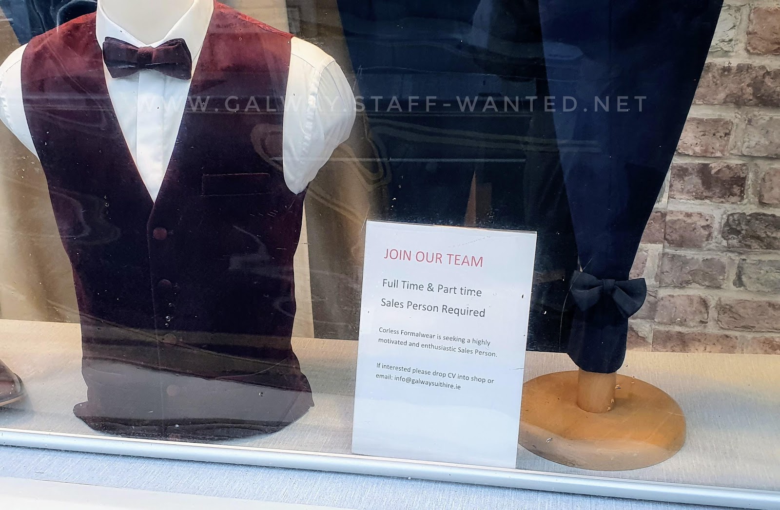 Mens formalwear shop window - manequin with maroon waistcoat, matching bow tie and white shirt - beside a staff-wanted advertisement