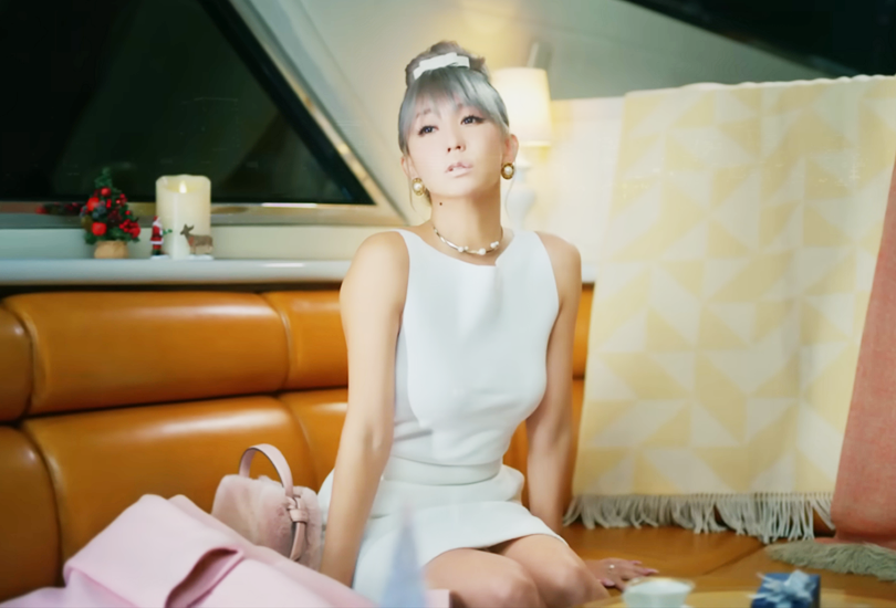 A screenshot from Koda Kumi’s music video for “Tooi Machi no Dokoka de...”. Featuring Kumi in close up, with her hands to her face, showing off her long pink nails.