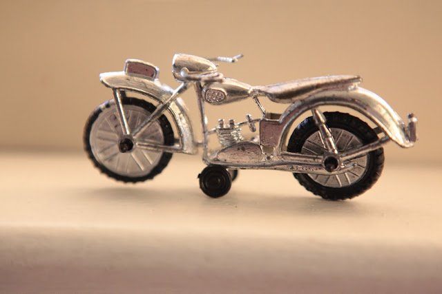 An old, silver, toy motorcycle sitting on a table. 