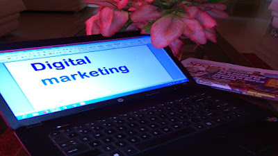 Blue digital marketing sign on a computer screen, red flowers, folded newspaper on a work table.