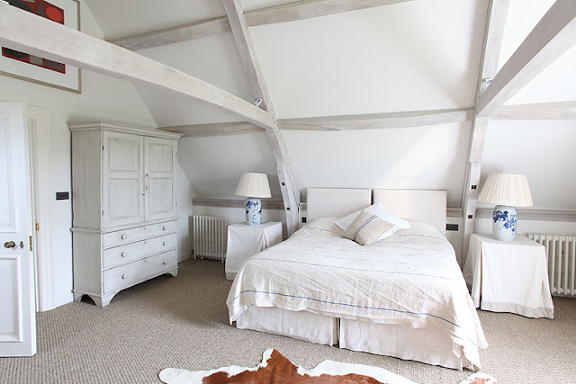 modern rustic bedroom with exposed beams, animal skin rug, carpeted floors, white wardrobe and two accent table with table cloth and matching lamps