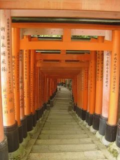 Stairs leading down and curving to the left. The stairs are in the middle of a series of red Torii gates with writing on them. Taken from the top of Fushimi-Inari in Japan