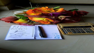 Black pen on white notepad, red flowers and a calculator on work table.