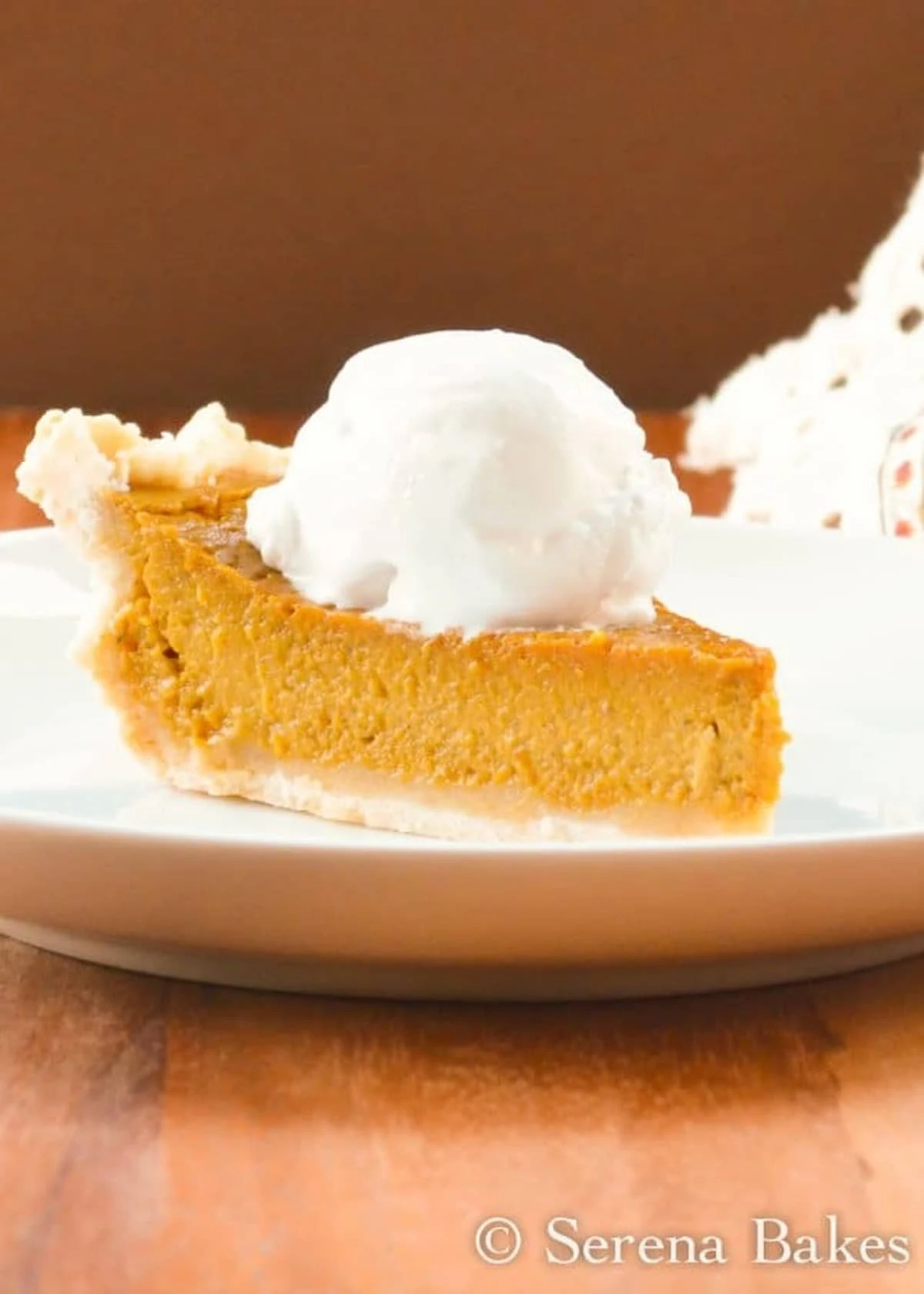 A side shot of Dairy Free Pumpkin Pie topped with Coconut Whipped Cream on a white plate.