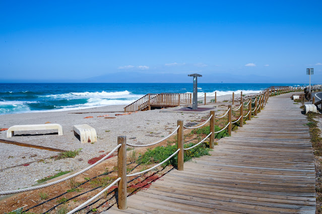 Paseo marítimo de madera, la arena de la playa y el las azules aguas del mar al fondo.