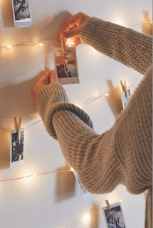 zoom of a woman's arms hanging pictures from twinkle lights hanging from a wall