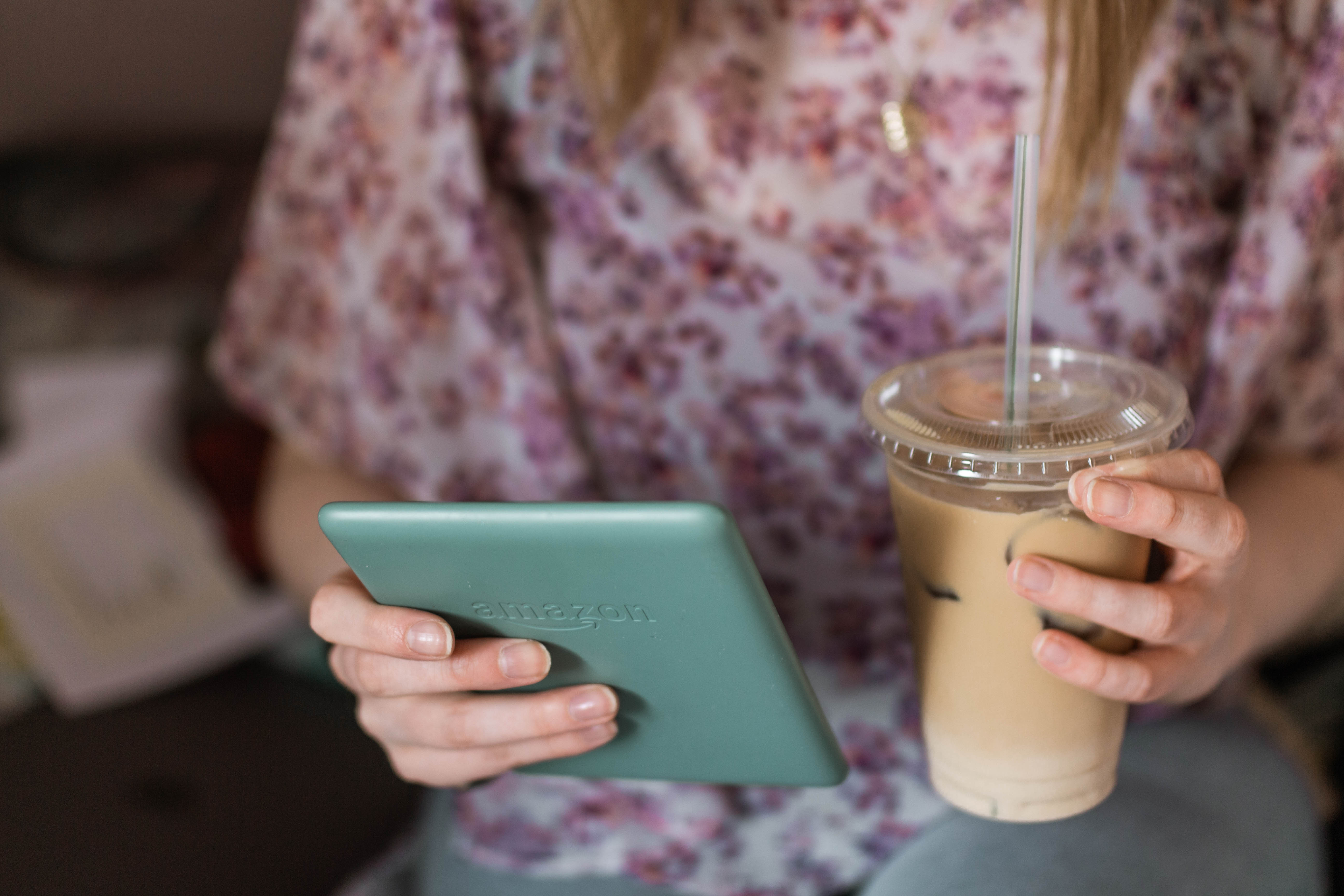 hands holding sage kindle paperwhite and iced coffee latte