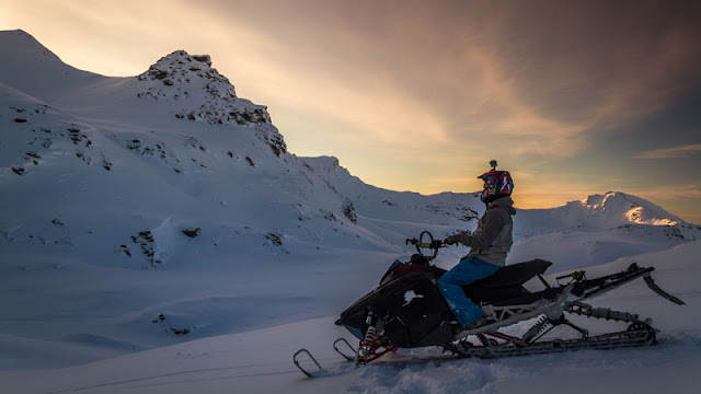 solo snowmobile rider watching the sun rise from behind the mountains