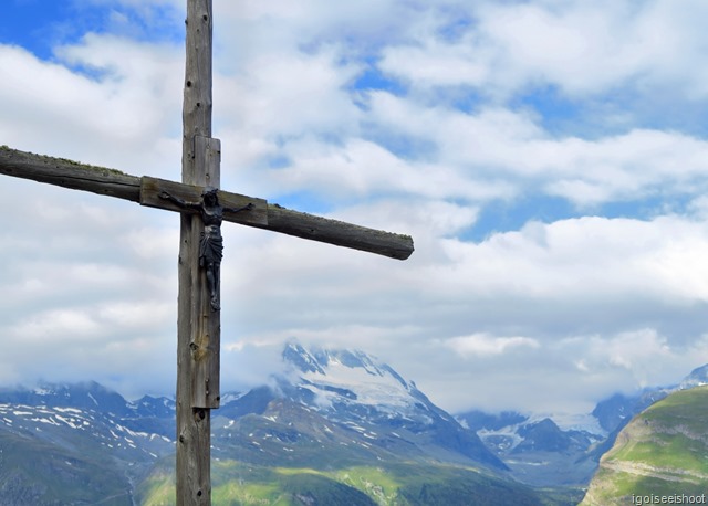 A wooden cross at Sunnegga, with the mountains and cloud covered Matterhorn in the back.