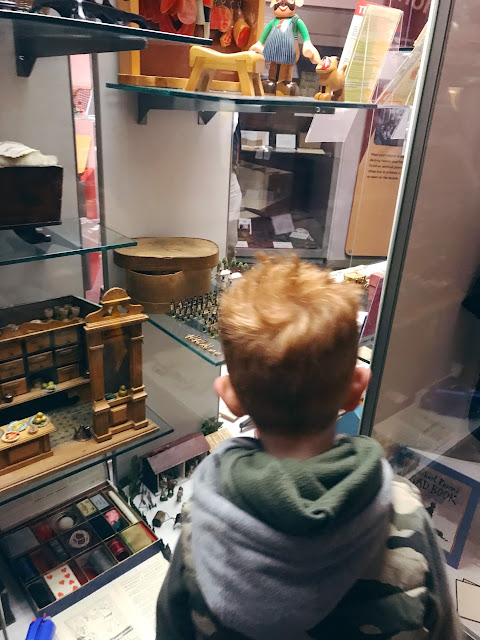 Little boy standing in front of a display case holding antique toys