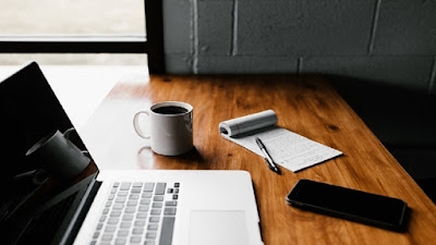 Online marketing work station with a computer, notepad and pen, a white mug of beverage and a smartphone.