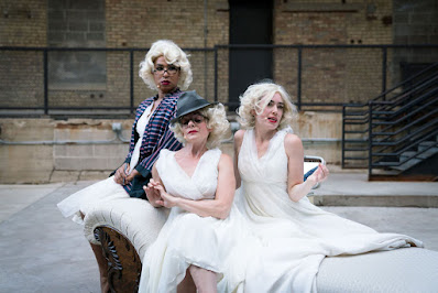 Three blonde women in white dresses on a chaise longe. they all resemble Marilyn Monroe.