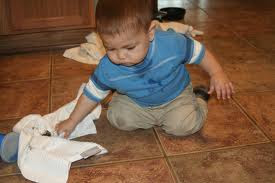 Toddler on the floor, with cloth in hand, wiping up something