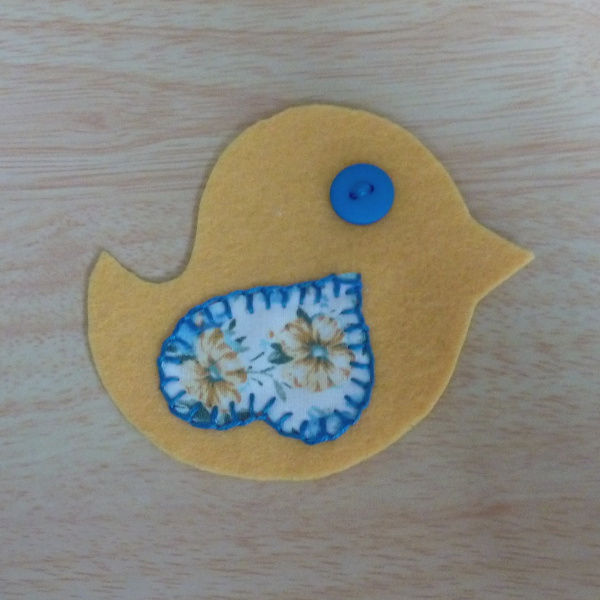 Yellow bird pattern piece with fabric wing sewn on and blue button eye