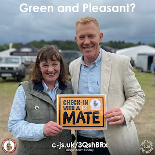 2 smiling people holding a poster for 'Check in with a mate' campaign. Text reads: Green and Pleasant?