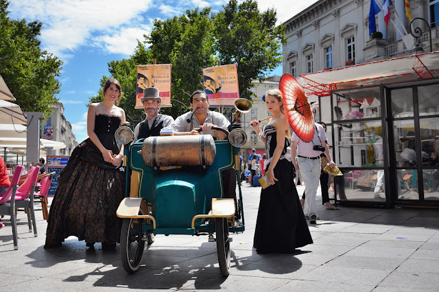  foto de uma carro antigo e moças e rapazes vestidos à moda antiga celebrando o festival de teatro de Avignon   