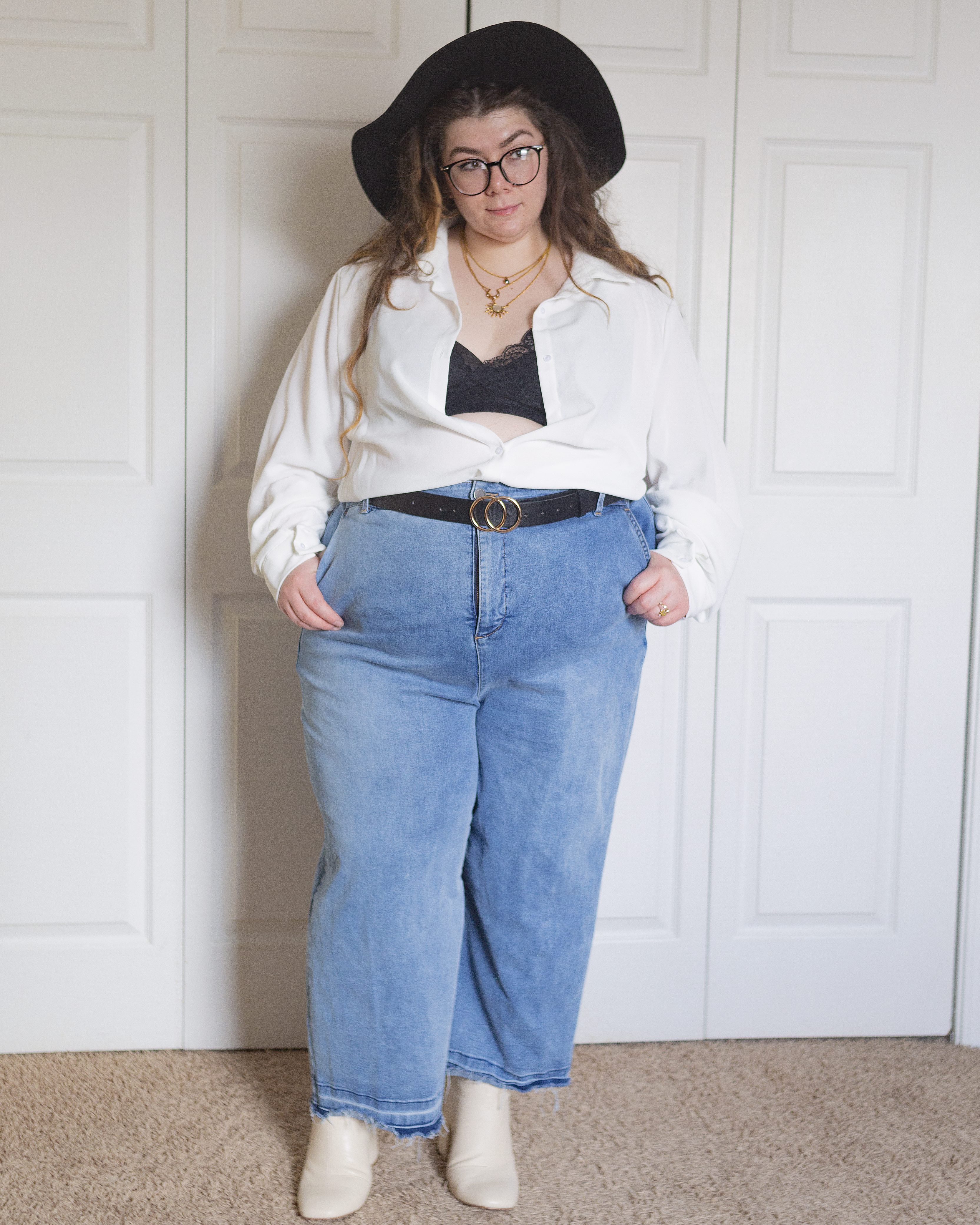 An outfit consisting of a white cotton button up blouse. unbuttoned to expose a bralette, tucked into light wash wide leg jeans and cream round toe boots.