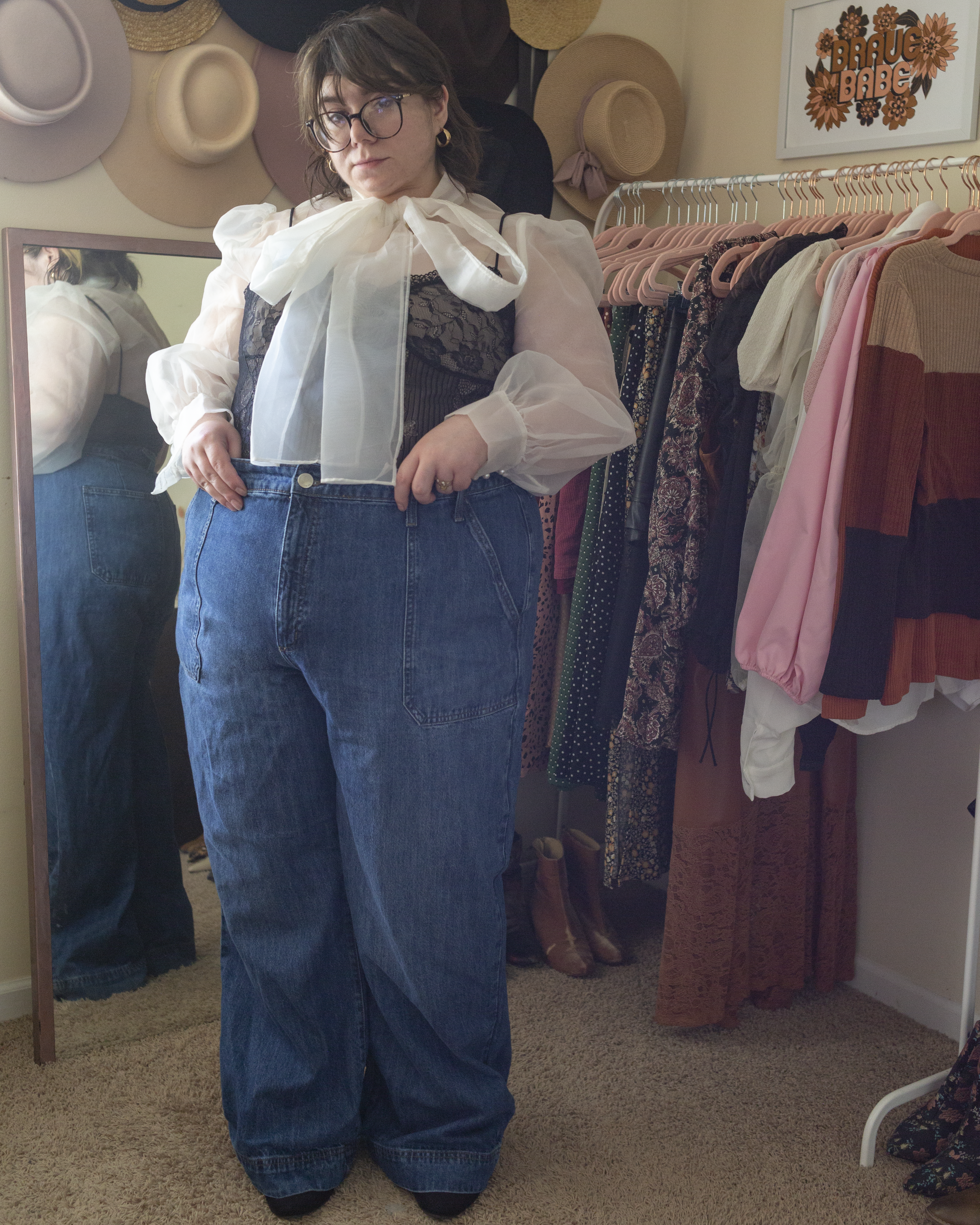 An outfit consisting of a black hat, a black lace camisole layered over a white blouse tucked into dark wash high rise wide leg jeans and black chelsea boots.