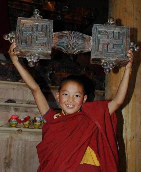 A boy wearing red robes holding a large wooden object with two swastikas.