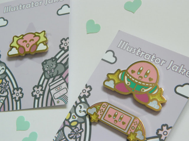 A photo showing three enamel pins by artist Illustrator Jake. They are all of Nintendo's Kirby 