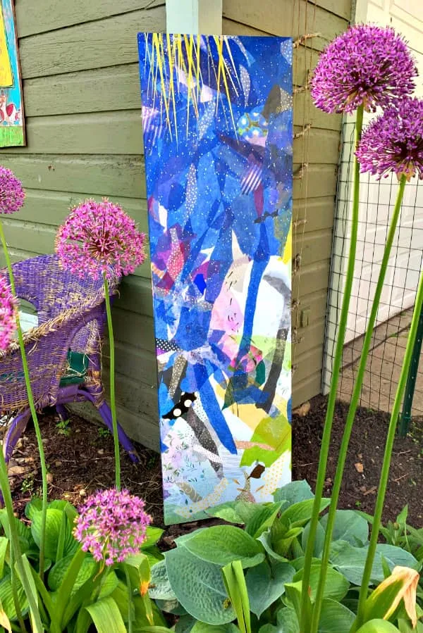 colorful paper art collage leaning against garage corner in allium flower bed