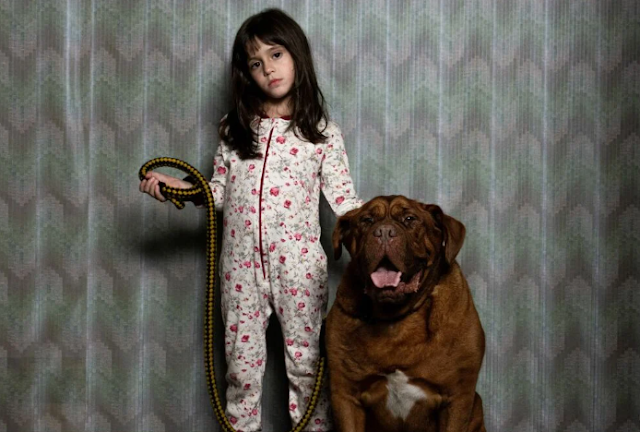 A girl in pajamas stands next to a dog