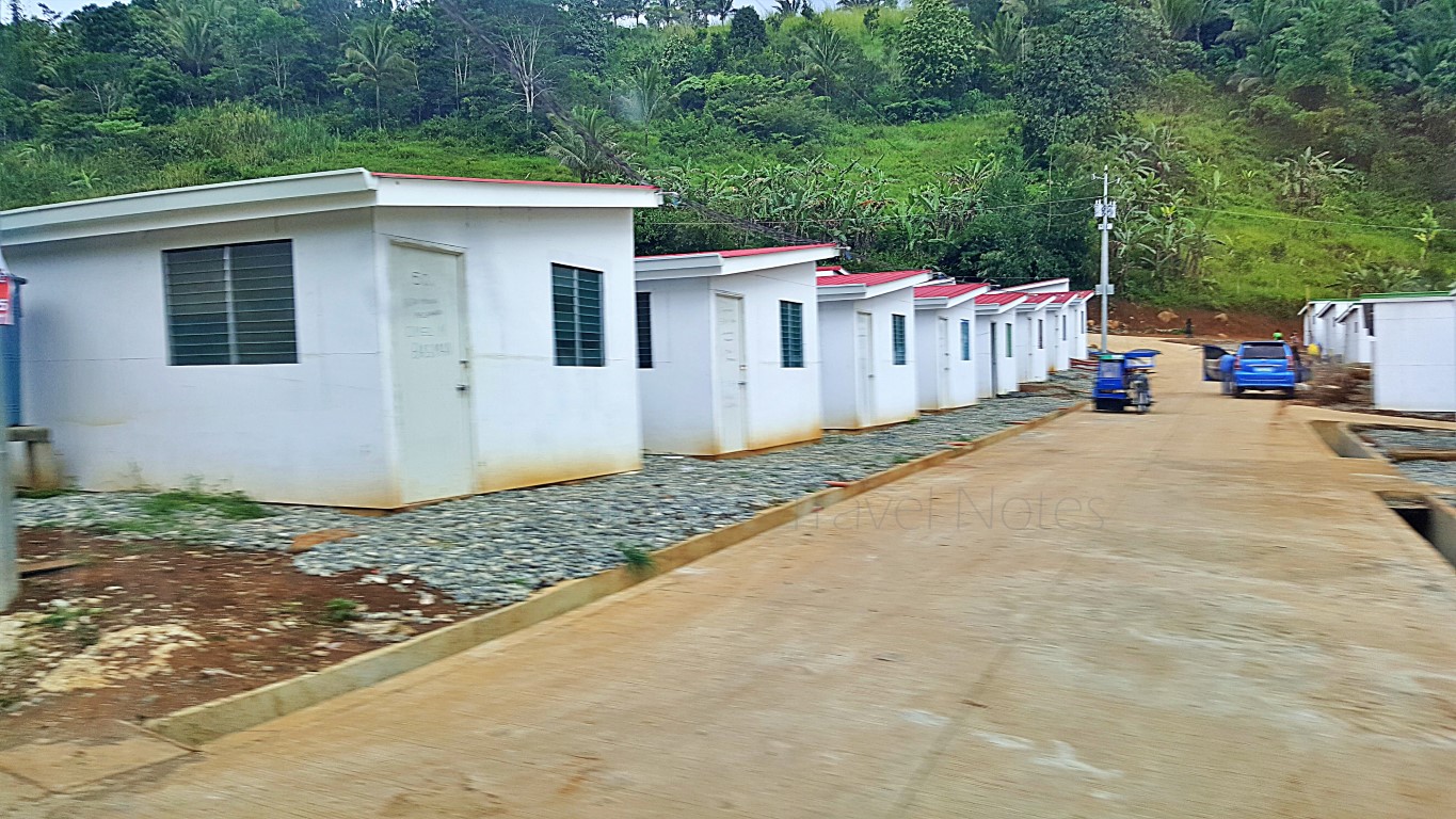 rows of newly built temporary shelters in uneven terrain