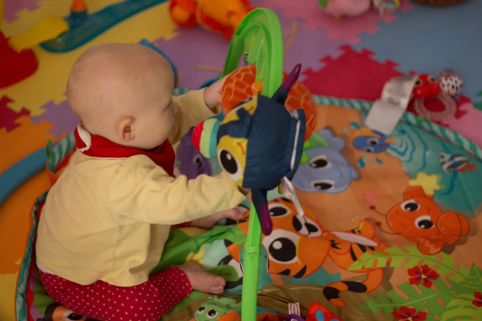 8 month old sitting up grabbing a mirror on an activity gym