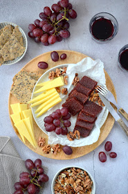Dulce de Membrillo, Weintrauben, Käse und Dinkel-Cracker sind auf einem Teller angerichtet. Daneben sind Walnüsse und zwei Gläser Rotwein zu sehen.
