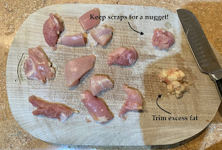 bite sized pieces of raw chicken thigh on a cutting board with a sharp knife