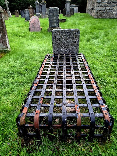 An ancient grave in a forest graveyard with a heavy iron, black painted latticework cage covering it. The grave of Seath Mor Sgorfhiaclach in a secluded area of the forest of Rothiemurc­hus estate, near Aviemore, Scotland