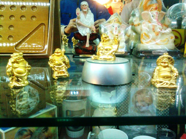 Sai Baba forms a backdrop to different Laughing Buddhas in various poses. They were deliberately placed thus!