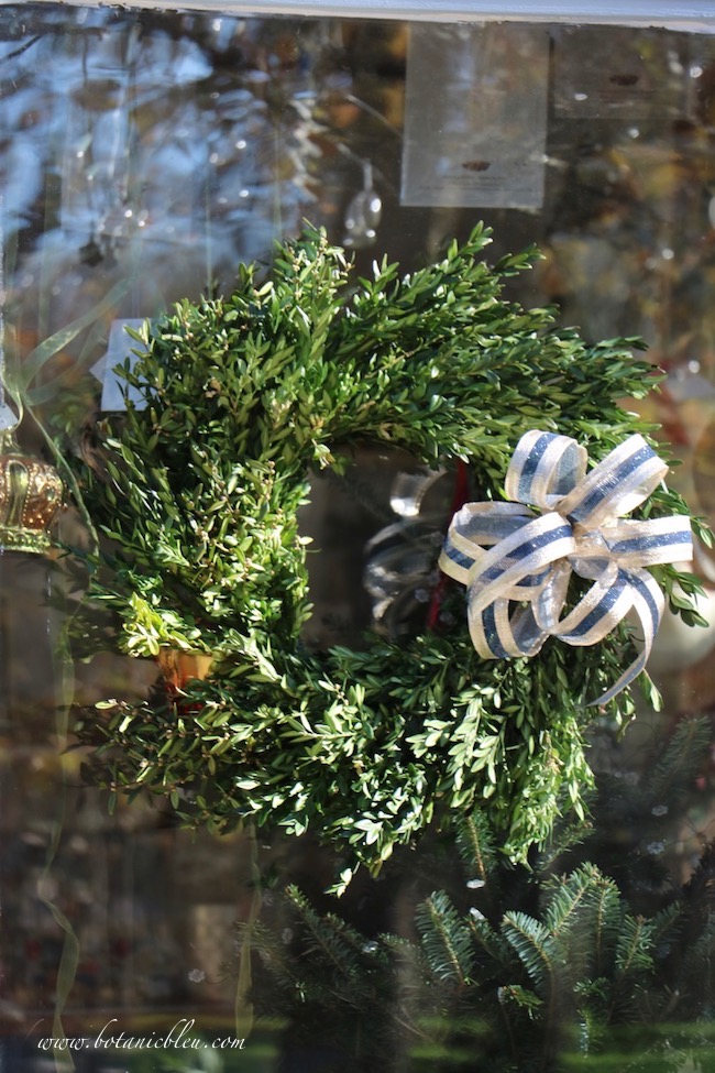 Wired gold and dark blue ribbon provides shimmer to wreaths on the French Country Christmas garden shed greenery