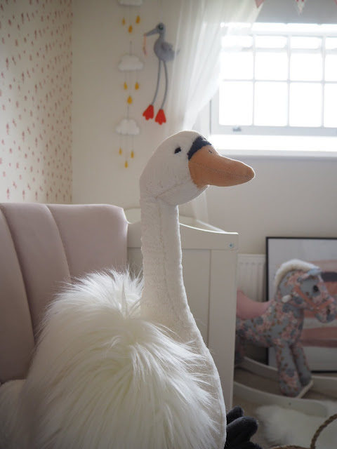 Nursery bedroom perfect for a baby girl toddler. Pink and swan ballet themed room with a sunburst mirror, feather lampshade, pom pom basket and liberty print rocking horse