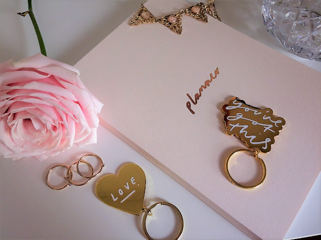 pink planner with pink peony next to it and gold keyrings and rings