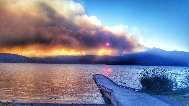 A dock in the foreground jets out into Diamond Lake. Smoke can be seen in the distance creating a beautiful sunset