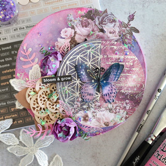 Prima Moon Child, Pretty Pale and Soprano flowers and lace trim; Tim Holtz Distress Spray Oxide and Stain in kitsch flamingo and dusty concord and Funky Floral dies; Scrapbook.com stickers and smart glue adhesives; Pinkfresh Essentials jewels