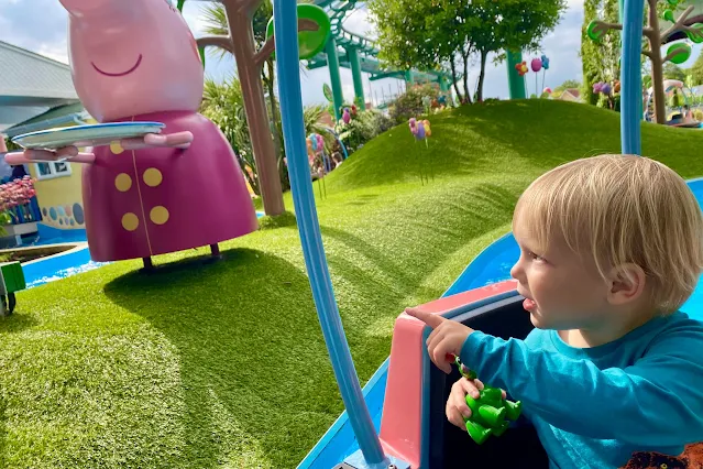 A toddler on a Peppa Pig World boat ride withe Peppa Pig characters visible