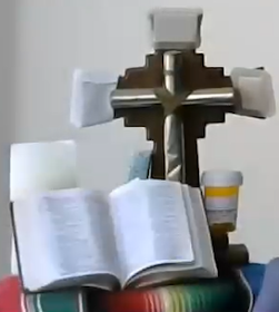 altar with a Bible, a candle, a cross with bandages on it, tissues, and a prescription bottle.