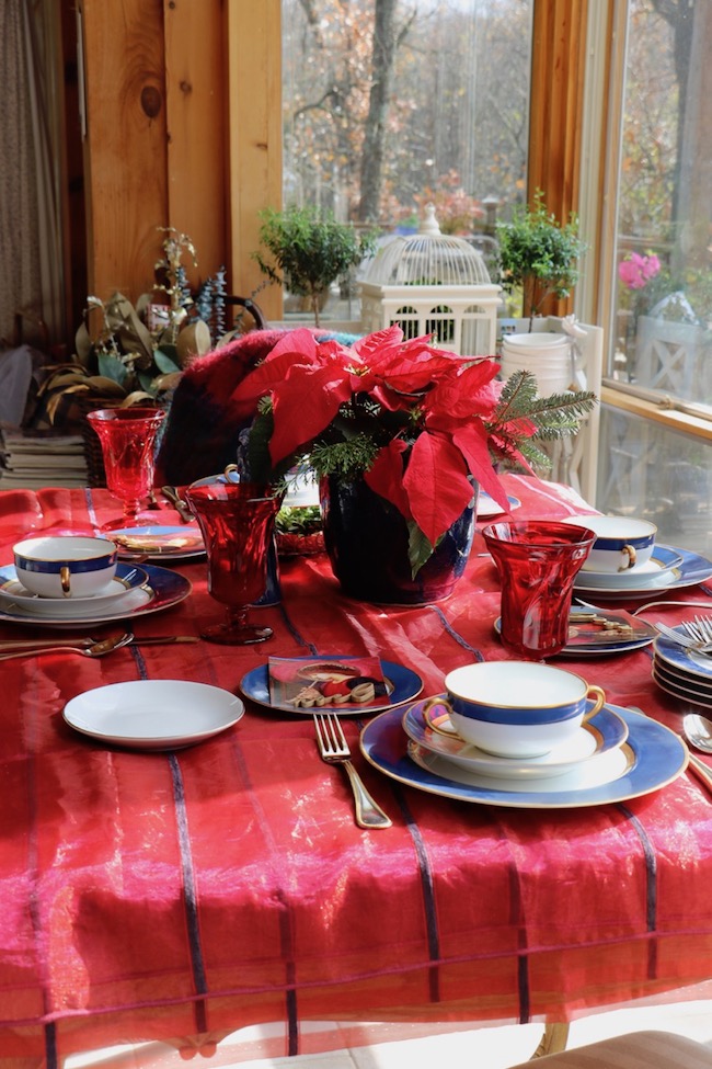 Red sheer, shimmering fabric with navy blue velvet stripes creates a festive tablecloth for a Christmas table setting