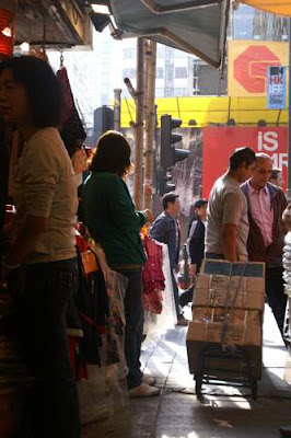 Image of a porter carrying goods by hand trolley and exiting an alley in Kowloon, Hong Kong.