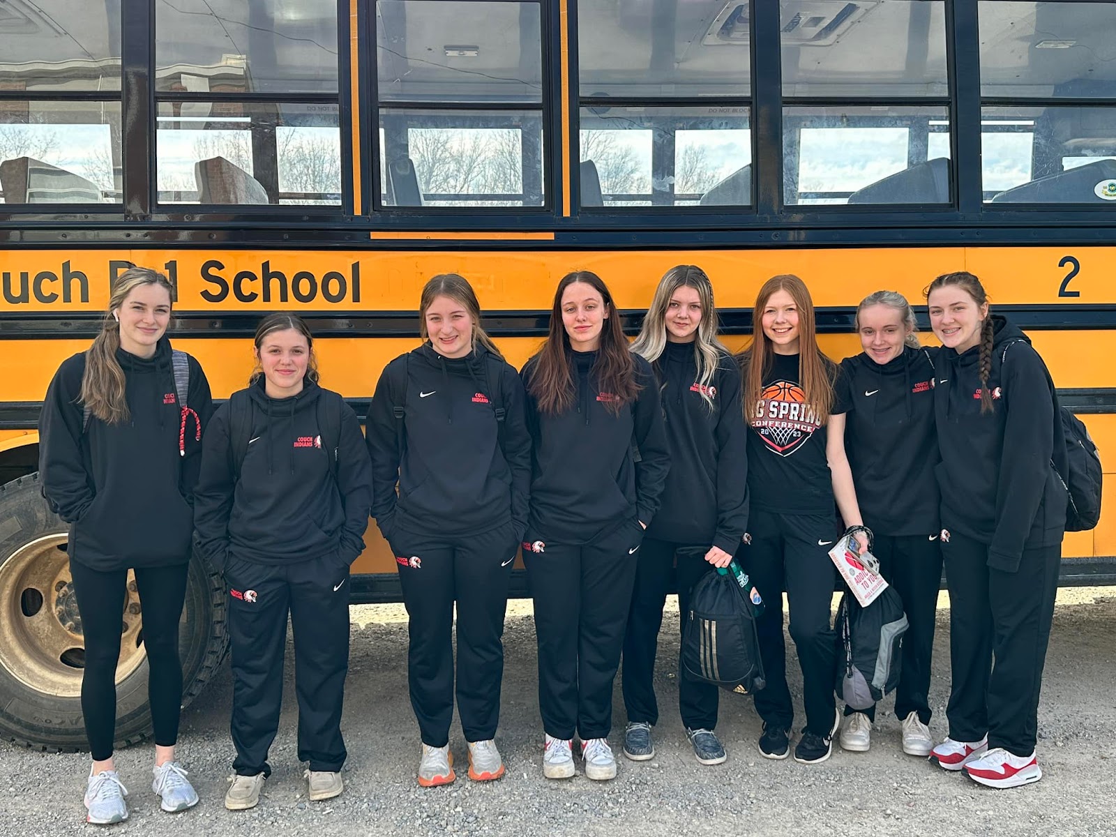 members of girls basketball team standing in front of school bus